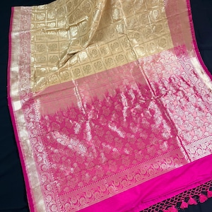May include: A gold and pink silk saree with a checkered pattern and floral designs. The saree has a gold border and a pink fringe.