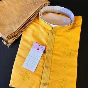 May include: A yellow kurta with gold embroidery and a white collar. The kurta is part of a set that includes a matching scarf. The tag on the kurta reads "KAASH COLLECTION House of Indian Ethnic Wear for Women, Men & Kids www.kaashcollection.com 415-827-4482 Sarees, Suits, Readymade Blouses, Dhupattas, Kurta Pajamas for Mens and Boys 405 Bowden Ct, Suite 200-L, Pleasanton, California 94588"