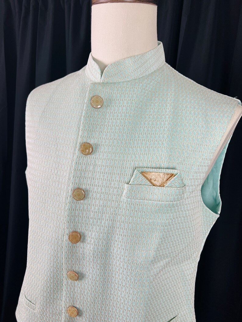 May include: A light blue sleeveless vest with a white and gold patterned design. The vest has a mandarin collar and six gold buttons down the front.