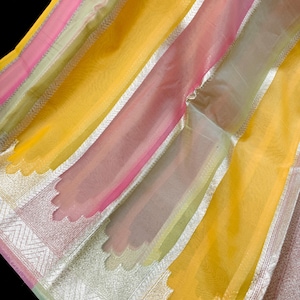 May include: A sheer fabric textile featuring vertical stripes in bright yellow, soft pink, and pale green. The fabric is accented with wide, metallic silver borders that display an intricate, scalloped edge pattern woven into the material.