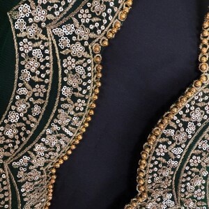 Peut inclure: Gros plan sur un v&ecirc;tement vert fonc&eacute; avec une broderie dor&eacute;e complexe. La broderie pr&eacute;sente des motifs floraux, des paillettes et de petites perles dor&eacute;es. Le design se d&eacute;tache sur un fond sombre.