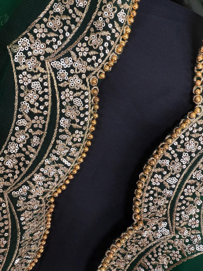 Peut inclure: Gros plan sur un v&ecirc;tement vert fonc&eacute; avec une broderie dor&eacute;e complexe. La broderie pr&eacute;sente des motifs floraux, des paillettes et de petites perles dor&eacute;es. Le design se d&eacute;tache sur un fond sombre.