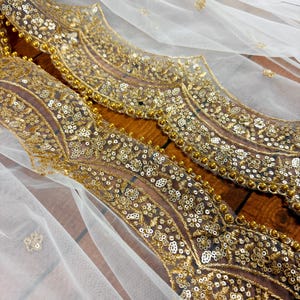 May include: White sheer fabric with a gold embroidered border. The border features a repeating pattern of floral motifs and sequins.