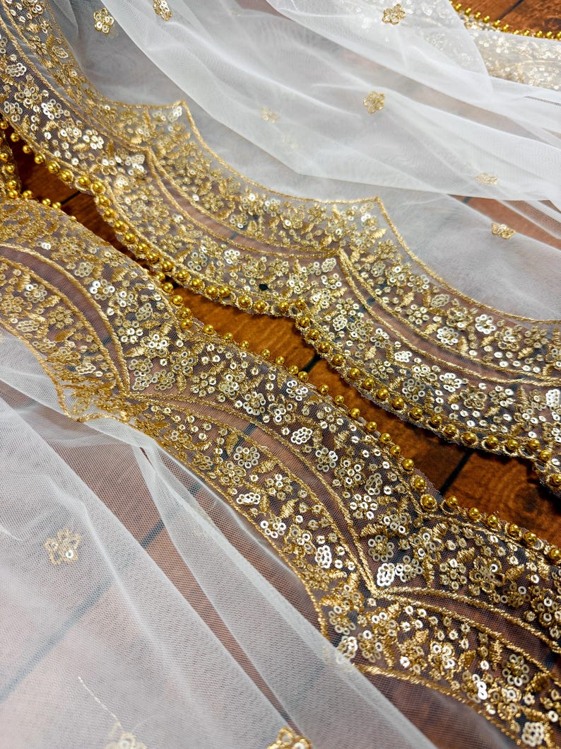May include: White sheer fabric with a gold embroidered border. The border features a repeating pattern of floral motifs and sequins.