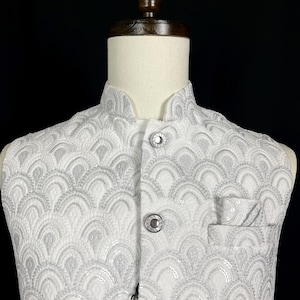 May include: White waistcoat with a silver sequin pattern and a pocket on the left side. The waistcoat has a mandarin collar and a button closure. The tag on the waistcoat reads "KAASH COLLECTIVE".