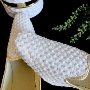 Pode incluir: Um par de sapatos brancos de tecido bordado com acabamento dourado. Os sapatos t&ecirc;m um tecido texturizado e uma palmilha confort&aacute;vel e acolchoada.