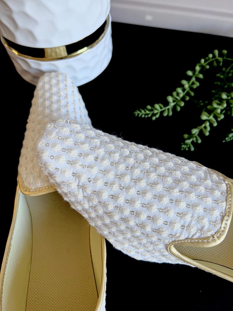 Pode incluir: Um par de sapatos brancos de tecido bordado com acabamento dourado. Os sapatos t&ecirc;m um tecido texturizado e uma palmilha confort&aacute;vel e acolchoada.
