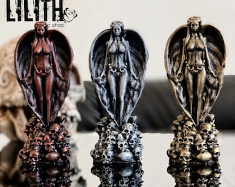 May include: Three statues of a winged female figure standing on a base of skulls. The statues are painted in different colors: red, silver, and gold.