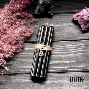 May include: A bundle of six black candles tied together with twine and a gold charm. The candles are on a dark wood surface.