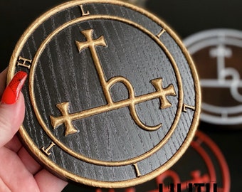 May include: A black wooden circle with a gold sigil of Lilith, a demon from the Lesser Key of Solomon. The sigil is surrounded by a gold circle with the letters "L I H I L" inscribed around it.