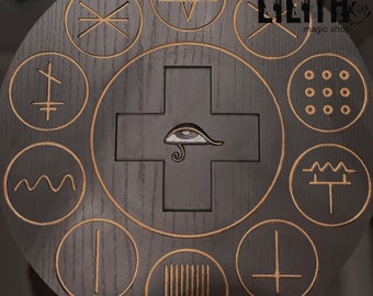 May include: A black wooden circle with a gold trim and various symbols engraved on it. The center of the circle features a white eye with a gold trim and a gold snake. The text "LILITH magic shop" is in the upper right corner of the circle.