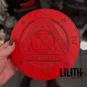 May include: A red wooden circle with a black sigil inscribed in the center. The sigil is surrounded by a triangle with the words "NEBOTOSOALEYE", "AKTIOPHIS", and "BRESHKIGAL" inscribed around it. The circle is decorated with black crosses and other symbols.