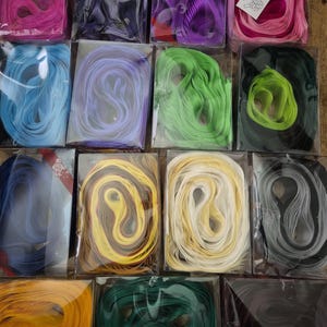May include: A selection of colourful ribbons in shades of pink, blue, green, yellow, and purple, packaged in clear plastic. The ribbons are arranged in rows, displaying a variety of colours and textures.