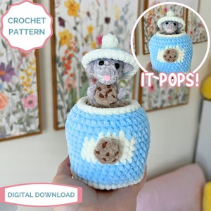 Op de afbeelding: Haakpatroon voor een blauwe en witte koekjespot met een grijze muis die uit de bovenkant kijkt. De muis houdt een bruine koek vast. De tekst "IT-POPS!" staat in wit op een blauwe achtergrond. De tekst "CROCHET PATTERN" staat in wit op een roze achtergrond. De tekst "DIGITAL DOWNLOAD" staat in wit op een roze achtergrond.