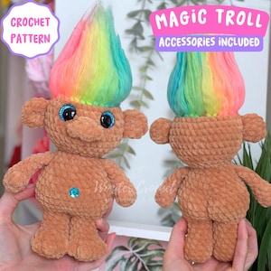 May include: Two crochet troll dolls with rainbow hair and blue glitter eyes. The dolls are brown with small arms and legs. Text on the image reads "CROCHET PATTERN" and "MAGIC TROLL ACCESSORIES INCLUDED".