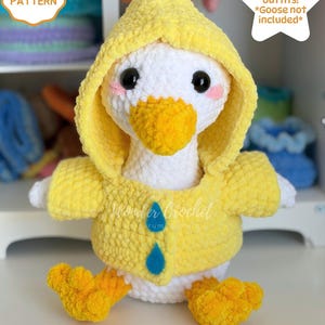 May include: A white crochet goose plush toy wearing a yellow hooded raincoat with two blue raindrop-shaped buttons. The goose has black eyes, pink cheeks, and an orange beak. Text on the image reads CROCHET PATTERN, 8 Seasonal outfits! *Goose not included*, and DIGITAL DOWNLOAD.