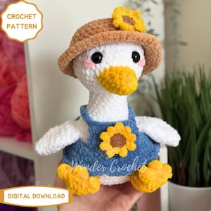 Peut inclure: Un adorable canard en crochet, portant un chapeau marron orn&eacute; d'un tournesol jaune et une salopette bleue avec un tournesol. Le canard a un bec et des pieds jaunes. Le texte "CROCHET PATTERN" et "DIGITAL DOWNLOAD" est visible.
