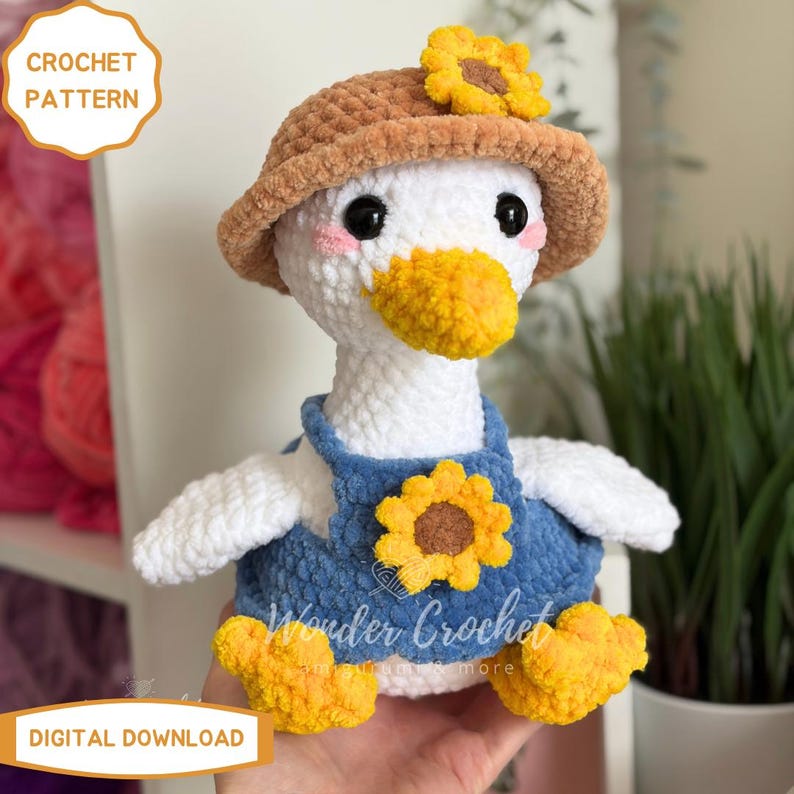 Peut inclure: Un adorable canard en crochet, portant un chapeau marron orn&eacute; d'un tournesol jaune et une salopette bleue avec un tournesol. Le canard a un bec et des pieds jaunes. Le texte "CROCHET PATTERN" et "DIGITAL DOWNLOAD" est visible.