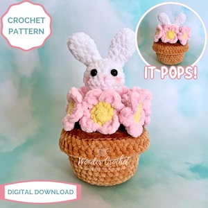 May include: A crocheted bunny emerging from a flower pot, surrounded by pink and yellow flowers. The bunny is white with black eyes and pink cheeks. The pot is brown. Text on the image says "CROCHET PATTERN", "IT POPS!", and "DIGITAL DOWNLOAD".