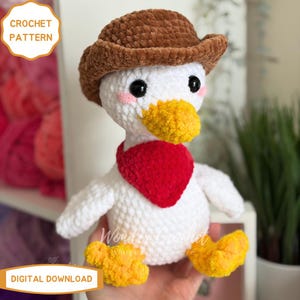 Peut inclure: Un canard blanc crochet&eacute; portant un chapeau de cowboy marron et un bandana rouge. Le canard a un bec et des pieds jaunes, avec des joues roses. L'image comprend le texte "CROCHET PATTERN" et "DIGITAL DOWNLOAD".