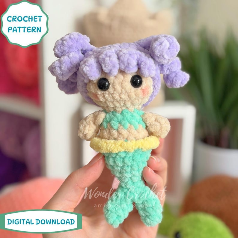 May include: Crocheted mermaid doll with purple hair, black eyes, and a turquoise tail. The doll has a light tan face and body, with a turquoise and yellow top. The image includes text that says "CROCHET PATTERN" and "DIGITAL DOWNLOAD".