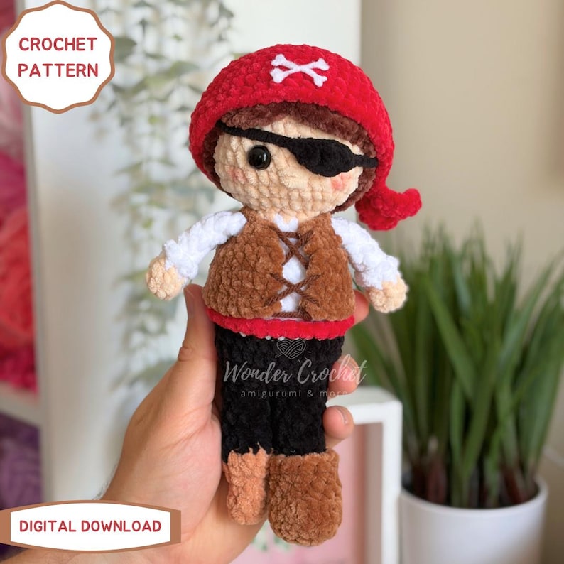 K&ouml;nnte beinhalten: Eine geh&auml;kelte Piratenpuppe mit rotem Kopftuch und wei&szlig;em Totenkopf-Symbol, schwarzer Augenklappe, brauner Weste mit Schn&uuml;rung, wei&szlig;en &Auml;rmeln und schwarzer Hose. Der Text CROCHET PATTERN und DIGITAL DOWNLOAD ist deutlich zu sehen.