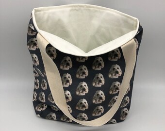 May include: A black canvas tote bag with a white dog face pattern. The bag has cream colored straps.