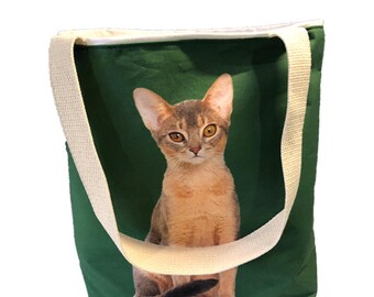 May include: A green canvas tote bag with a white strap and a printed image of a brown Abyssinian cat.