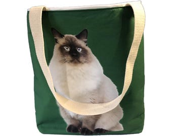 May include: A green canvas tote bag with a white cat printed on the front. The cat has blue eyes and a white body with brown markings.