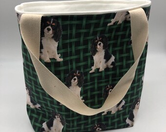 May include: A green and black canvas tote bag with a white fabric handle. The bag features a repeating pattern of Cavalier King Charles Spaniels.