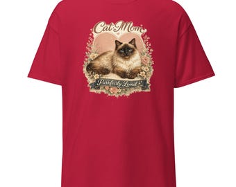 May include: A red short-sleeved t-shirt featuring a graphic of a Siamese cat lying down inside a heart shape surrounded by flowers. The text "Cat Mom" appears above the cat, and a banner below reads "Purrfectly Loved" in a decorative font.