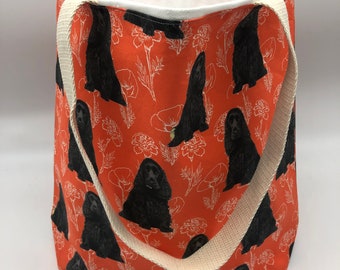 May include: Orange canvas tote bag with white floral and black dog silhouettes. The bag has two white canvas straps.