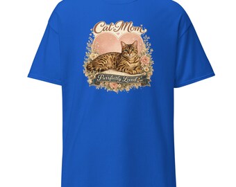 May include: A royal blue short-sleeve t-shirt featuring a graphic print of a brown tabby cat resting in front of a large heart. The design includes floral accents, the text Cat Mom at the top, and the text Purrfectly Loved on a banner below.