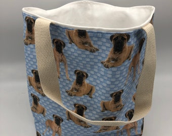 May include: A blue canvas tote bag with a white lining and cream-colored straps. The bag is decorated with a repeating pattern of brown bullmastiff dogs on a blue and white checkered background.