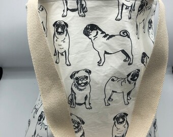 May include: A white canvas tote bag with black pug silhouettes printed all over. The bag has a cream-colored canvas strap.