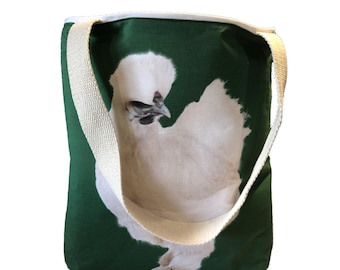 May include: A green canvas tote bag with a white chicken printed on the front. The bag has white straps.