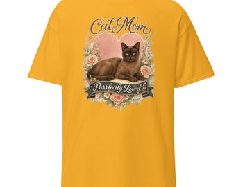 May include: A mustard yellow t-shirt featuring a graphic of a brown cat lying down in front of a pink heart and floral arrangement. The text reads Cat Mom at the top and Purrfectly Loved on a dark banner at the bottom of the illustration.
