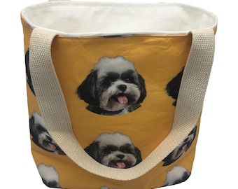 May include: A yellow canvas tote bag with a repeating pattern of a dog's face. The dog has black and white fur and is sticking its tongue out. The bag has two cream-colored straps.