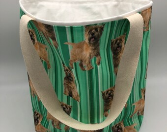 May include: A tote bag with a green striped pattern featuring images of Cairn Terriers. The bag has cream-colored handles and a white interior. The bag is designed for carrying items.