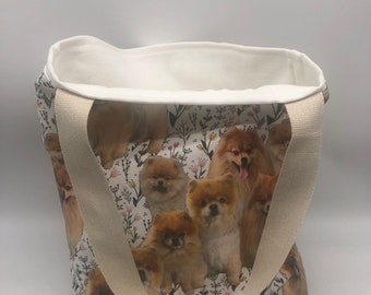 May include: A white canvas tote bag with a floral pattern and images of Pomeranian dogs. The bag has two cream-colored straps.