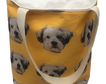 May include: A yellow canvas tote bag with a white dog face pattern. The bag has two long, cream-colored straps.