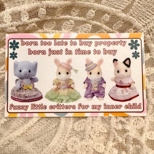 May include: A rectangular sticker with the text "born too late to buy property, born just in time to buy" and "fuzzy little critters for my inner child." The sticker features four small animal figurines in dresses and suits.