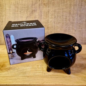 May include: A black cauldron oil burner with three legs, two handles, and star accents. The burner has a round opening for a candle and a top for oil or wax. The box reads "Cauldron Oil Burner."