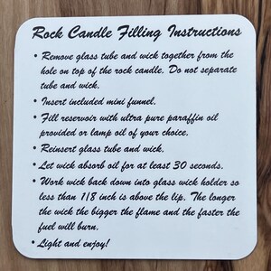 May include: White card with black text outlining instructions for filling a rock candle. The instructions include removing the glass tube and wick, inserting a funnel, filling the reservoir with paraffin oil, reinserting the tube and wick, letting the wick absorb oil for 30 seconds, working the wick down into the holder, and lighting the candle.