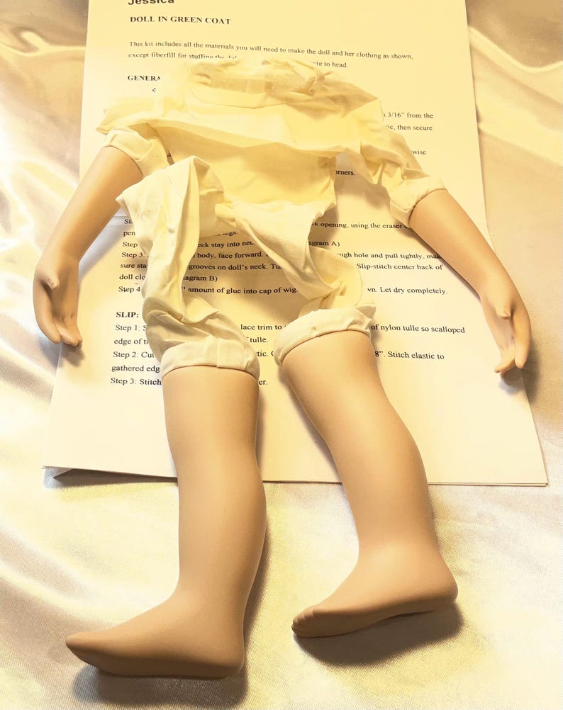 May include: A doll kit with a doll's body, arms, and legs, partially assembled. The doll is wearing a cream-colored dress. The kit includes instructions and materials for completing the doll, with text that reads "DOLL IN GREEN COAT".
