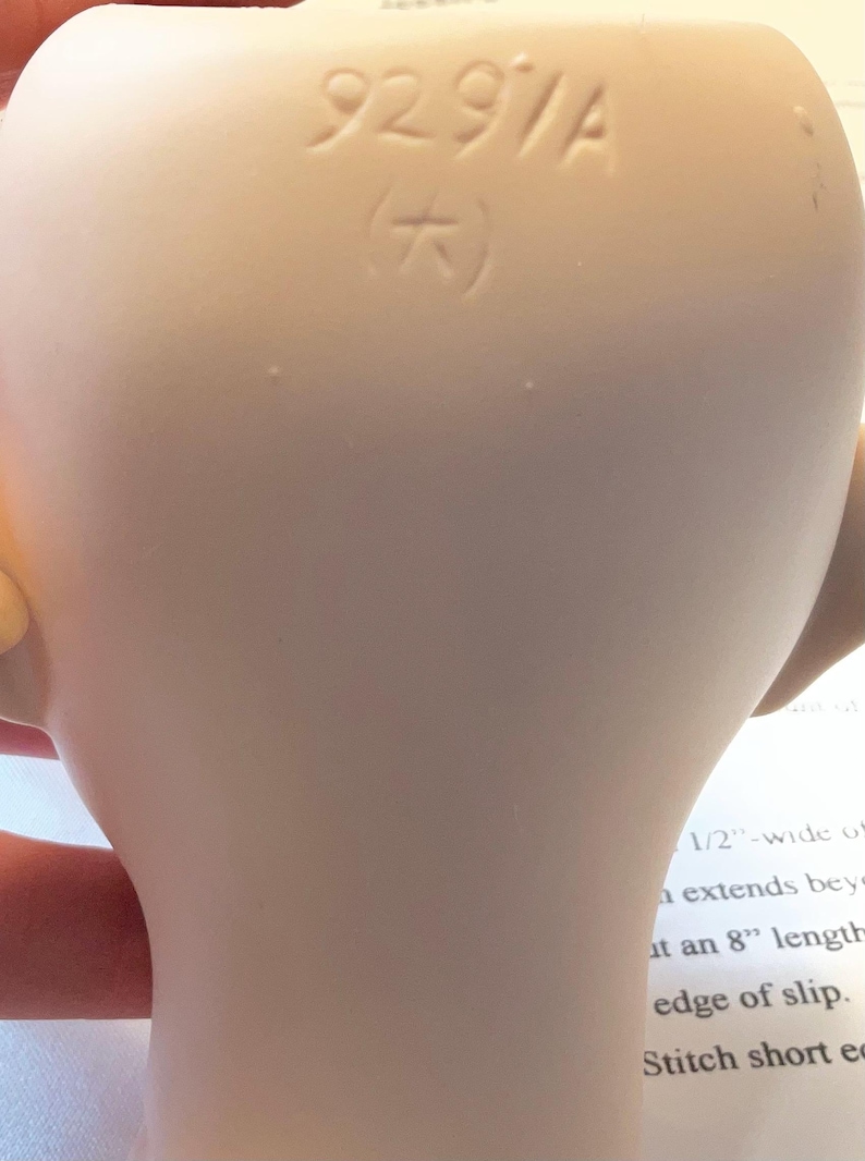 May include: Close-up of a pale, smooth ceramic object with the stamped text "9291A" and a symbol. The object has a curved shape and appears to be part of a larger item. The background includes text.