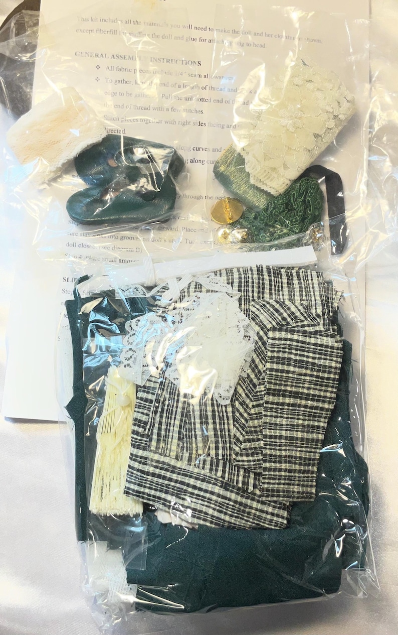 May include: A doll-making kit containing various fabric pieces, lace, and small accessories. The kit includes a green and white plaid fabric, green fabric, and a pair of green doll shoes. Instructions are visible in the background.
