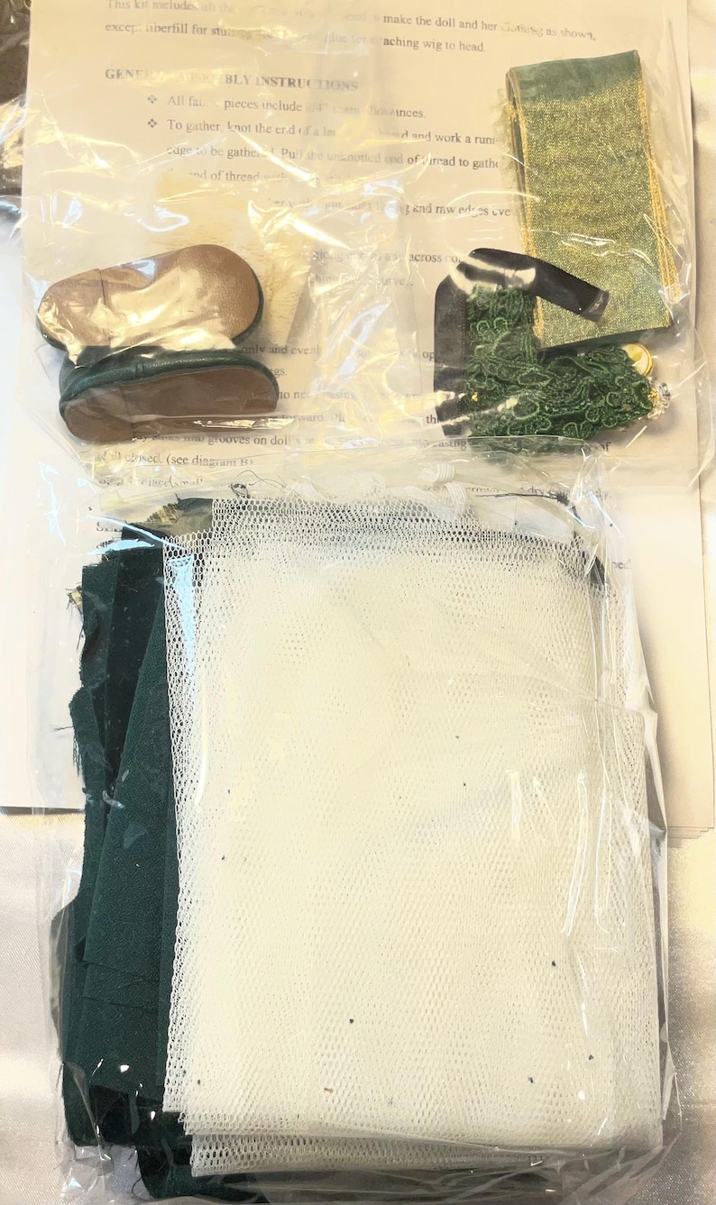 May include: A doll-making kit with various components visible through clear packaging. Includes small doll shoes, green fabric, a white mesh, and other accessories. The kit appears to contain materials for creating a doll.