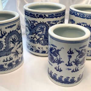 May include: Four white ceramic containers with blue dragon and wave designs. The containers vary in size and shape, with a cylindrical form and a wide opening. The blue and white color scheme gives them a classic, decorative look.