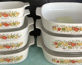 Op de afbeelding: Een set van zes witte ovenschaaltjes met deksels. De schaaltjes hebben een bloemmotief met groene bladeren, rode en gele vruchten en de tekst "Le Chateau".